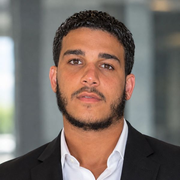 Man with short curly hair and beard in black suit.
