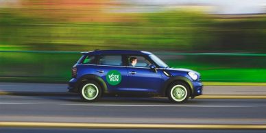 Blue car with a green logo driving fast.