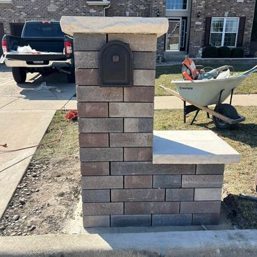 A brick mailbox structure with a bench in front of a house under construction.