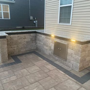 Outdoor stone patio with built-in counter and lighting by a house.