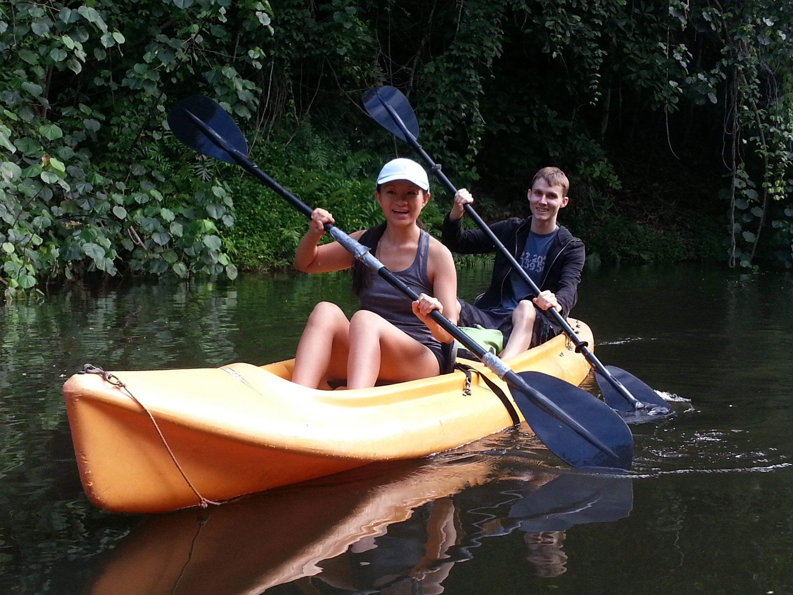 Two paddlers enjoying a tandem kayak beside lush river vegetation on Kauai