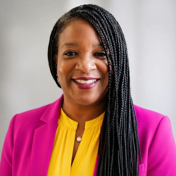 Smiling woman with braided hair wearing bright pink blazer and yellow top.