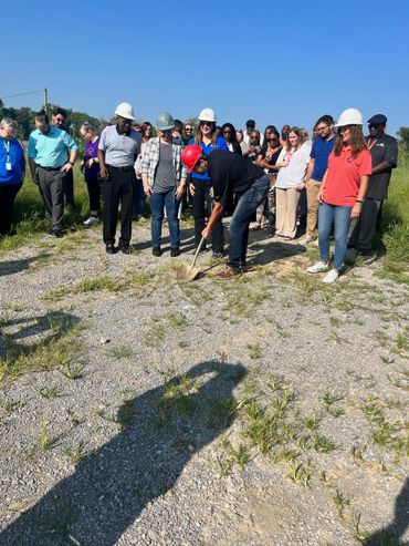 Group of people with hard hats at a groundbreaking ceremony on a sunny day.