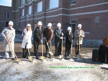Seven people in hard hats at a groundbreaking ceremony with golden shovels.