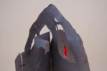 Top pointed section of metal sculpture with rough holes. Two filled with red and blue stained glass