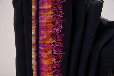 Cross stitch in magenta, orange, pink and yellow on black, in horizontal bars of different lengths