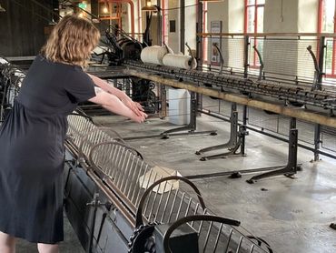 The artist holds cassette tape which has been stretched over spinning mule in place of yarn