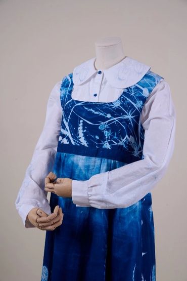 Long apron dyed deep blue with teasel plant design. Worn on mannequin over white embroidered blouse
