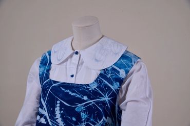 Close up of top of outfit showing collar, buttons and sleeves of blouse under yoke of blue apron