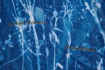 Detail of cloth dyed blue with shadowy silhouettes of plants. Two names written amongst the pattern