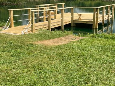 A wooden dock extends over a calm lake with green grass in the foreground.