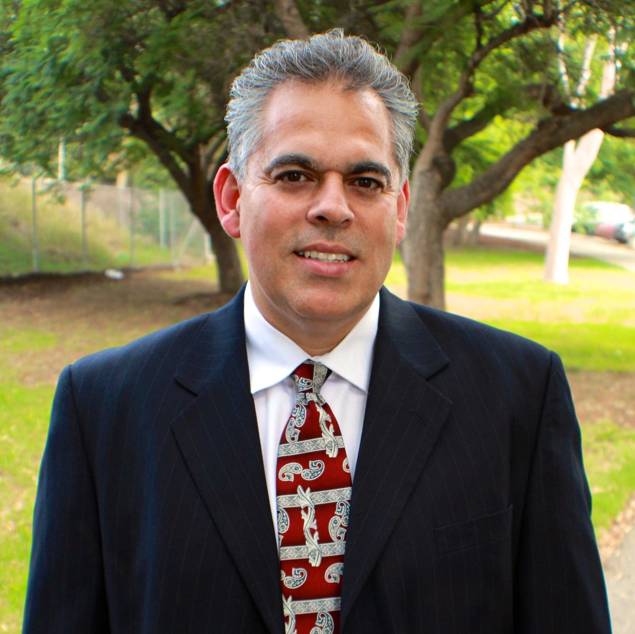 Man in suit outdoors with trees in background.