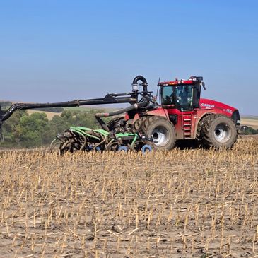 Large red tractor working on a dry field under clear blue sky.