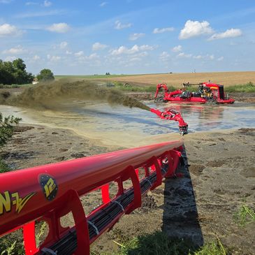 A red agricultural machine spraying liquid on farmland under a blue sky.