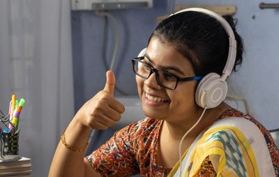 A cheerful woman wearing headphones gives a thumbs up.