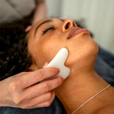 Woman receiving a facial massage with a white gua sha tool.