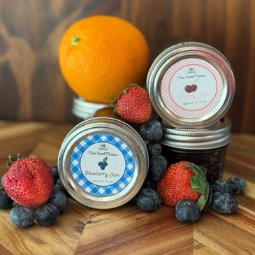 Assorted jams with fresh fruits on wooden surface.