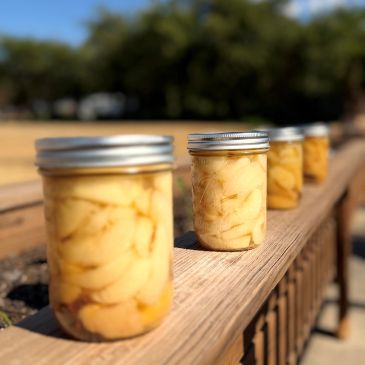 Four jars of preserved fruit lined up on a wooden railing.