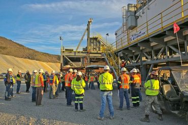 Construction workers in safety gear gather outdoors for a meeting at an industrial site.