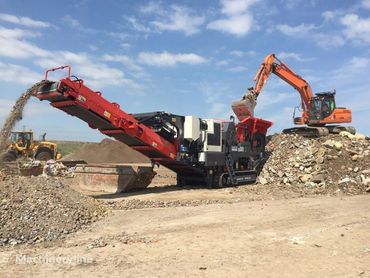 Excavator loading debris into a mobile crusher at a construction site.