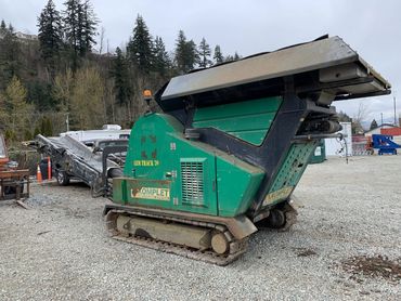 Green industrial Komplet recycling machine with tracks on gravel.