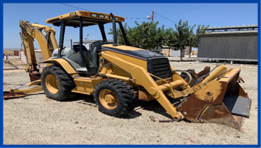 Yellow backhoe loader parked on a dirt lot under clear skies.