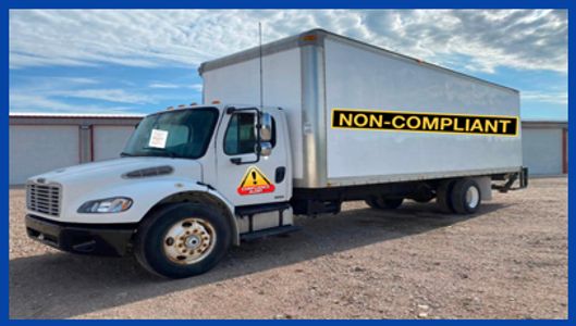 White truck with a large 'NON-COMPLIANT' sign on its side.