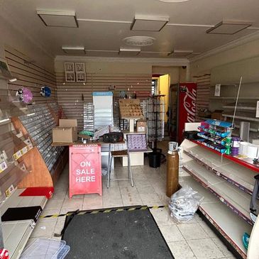 Interior of a small, cluttered retail store with empty shelves and sale signs.