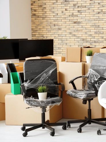 Office chairs wrapped in plastic with boxes and monitors in a modern workspace.