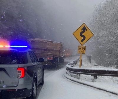 Police car with flashing lights next to a snowy winding road sign.
