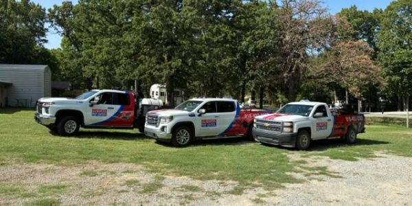 Three pickup trucks with company logos parked on grass.
