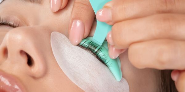 Applying eyelash extensions with a tool on closed eyes.