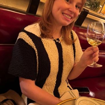 A woman smiling and holding a glass of white wine in a cozy restaurant.