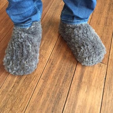 Feet in cozy gray fuzzy slippers on wooden floor.