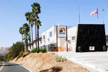 Sequoia Village building with palm trees and an American flag under a clear sky.