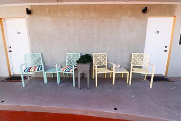 Two colored chairs and tables with room numbers in front of white doors.