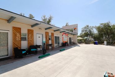 Outdoor seating area and electric vehicle charging spot beside a white building under clear blue sky.