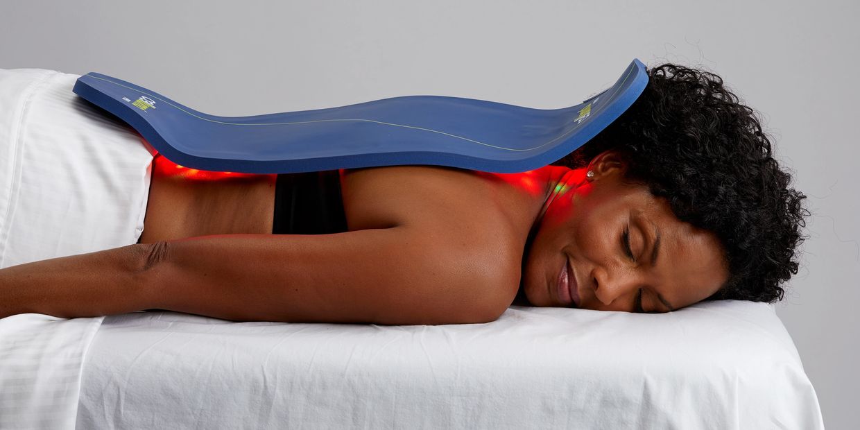 Black woman laying face down on massage table with LED light therapy panel placed over back.
