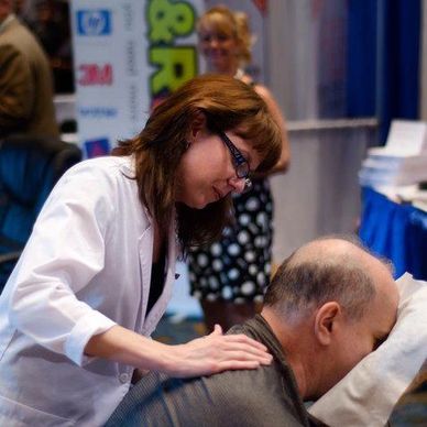 Diane performing Tuina (Chinese bodywork) on male volunteer in massage chair.