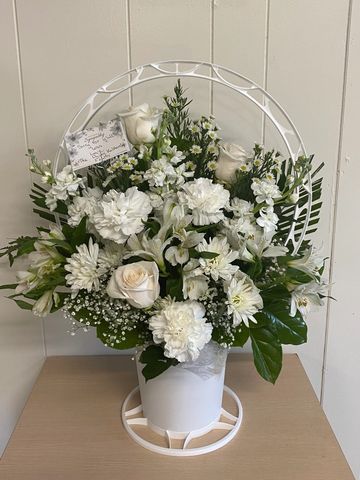 Elegant white floral arrangement in a white pot with green leaves.