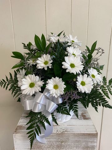 White daisies with green foliage in a basket, adorned with a silver ribbon.