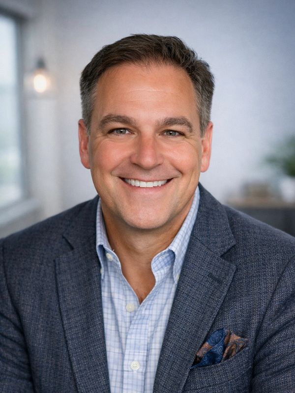Smiling man in a blue blazer and checked shirt.