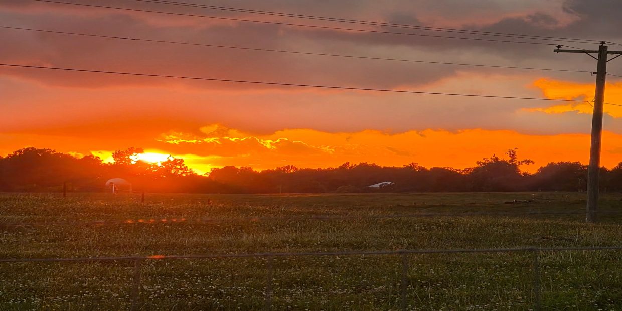 Vibrant orange sunset over a rural field with power lines.