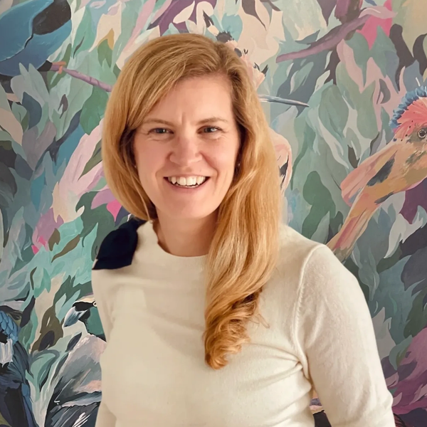 Smiling woman with long blonde hair in front of a colorful bird mural.