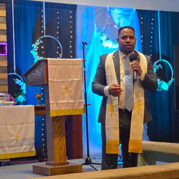 Man speaking in a church wearing a white stole.