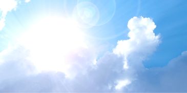 Bright sun shining through fluffy clouds in a blue sky.