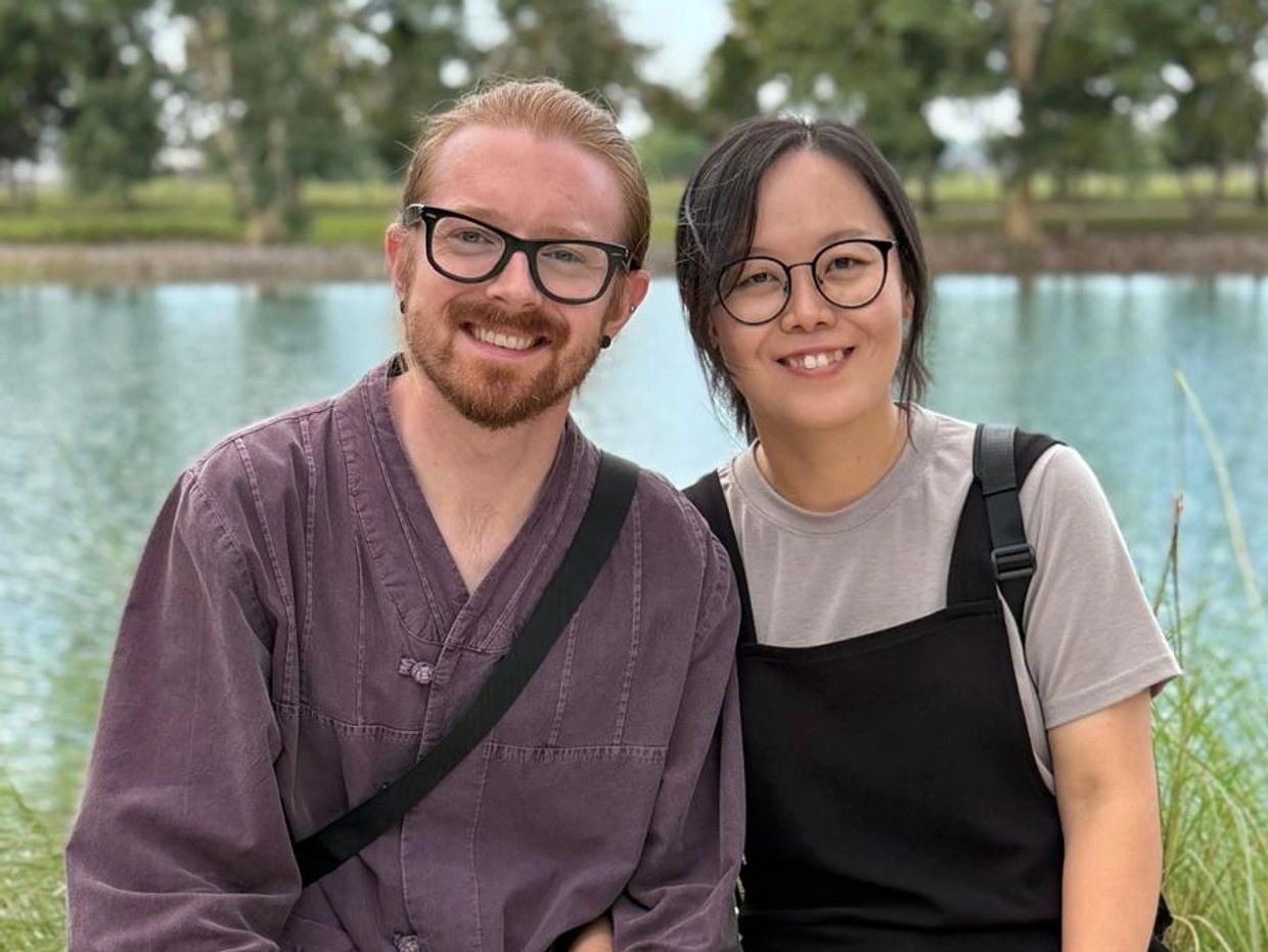 A smiling couple wearing glasses by a lake.
