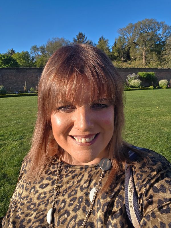 Smiling woman outdoors on a sunny day in a leopard print top.