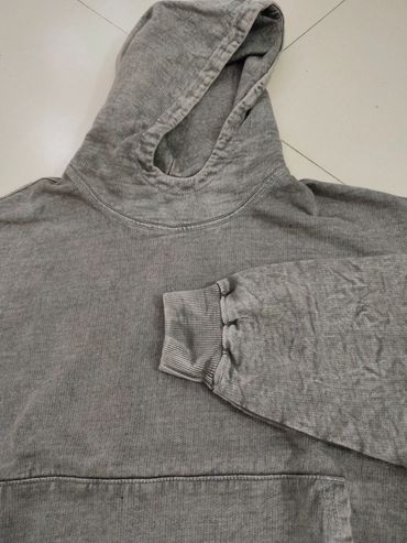 A gray hoodie with ribbed cuffs laid flat on a tiled floor.