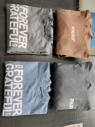 Four folded sweatshirts with printed text on a dark surface.